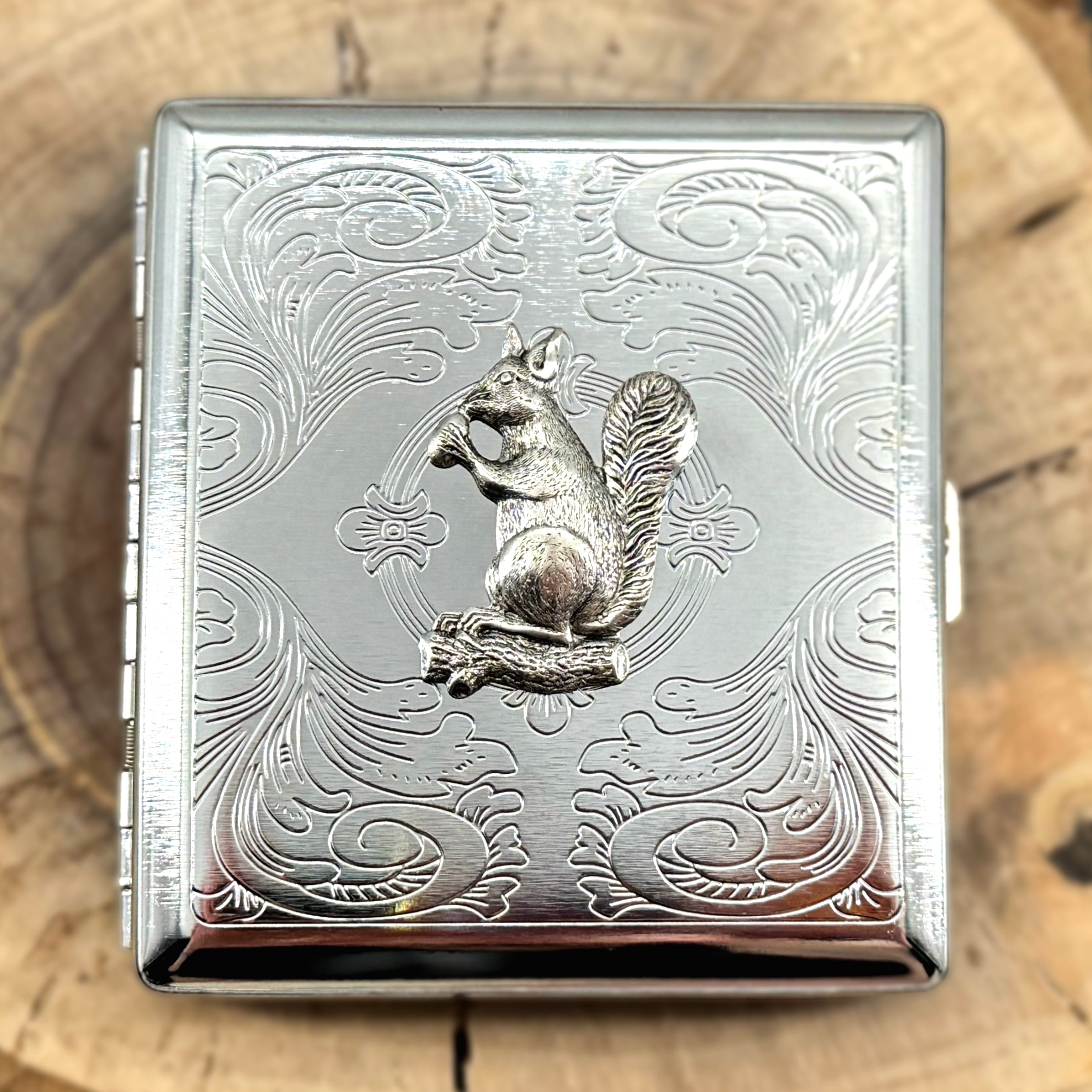 Silver metal cigarette case with raised squirrel design and ornate scrollwork