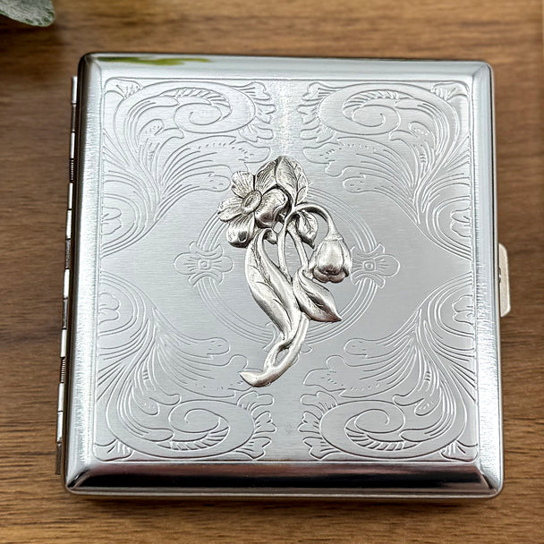 Bluebell metal cigarette case featuring a stylized bluebell and blossom on an ornate stamped scrollwork background