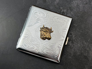 Close-up of detailed bronze cow head on stamped metal scrollwork background.