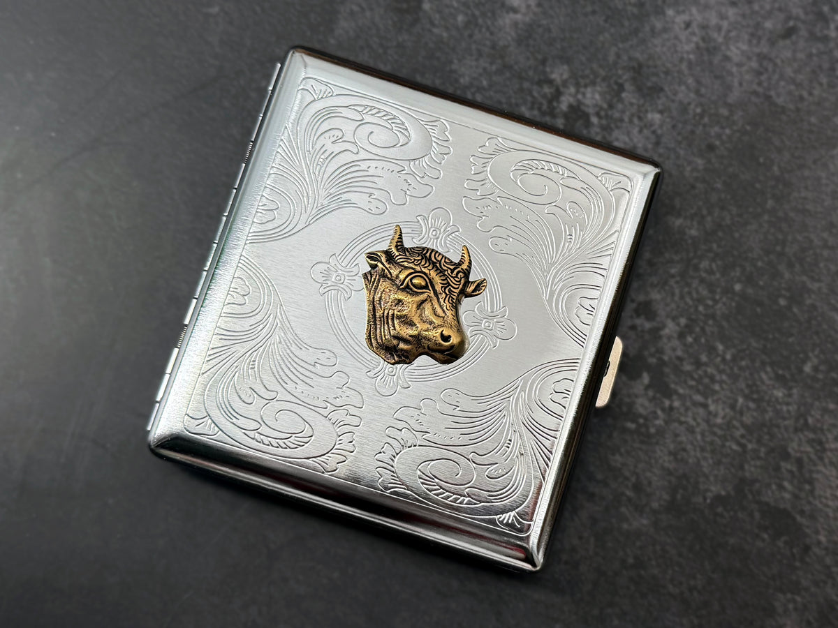 Close-up of detailed bronze cow head on stamped metal scrollwork background.