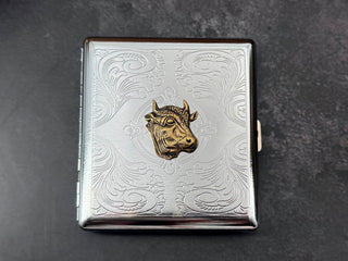 Front view of Western cow cigarette case with decorative silver scrollwork.