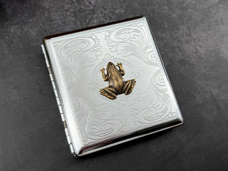 Angled view of handmade metal cigarette case with raised amphibian design.