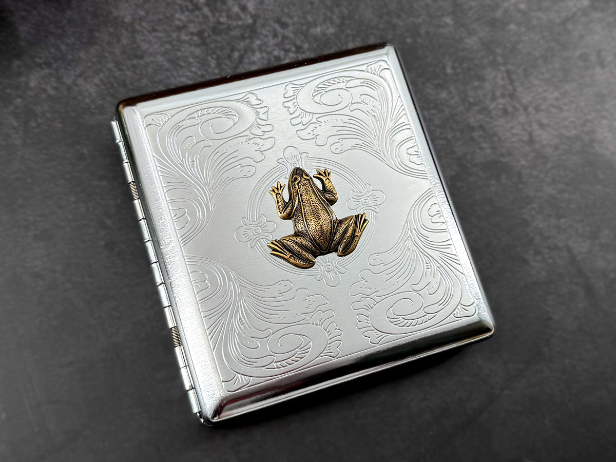 Angled view of handmade metal cigarette case with raised amphibian design.
