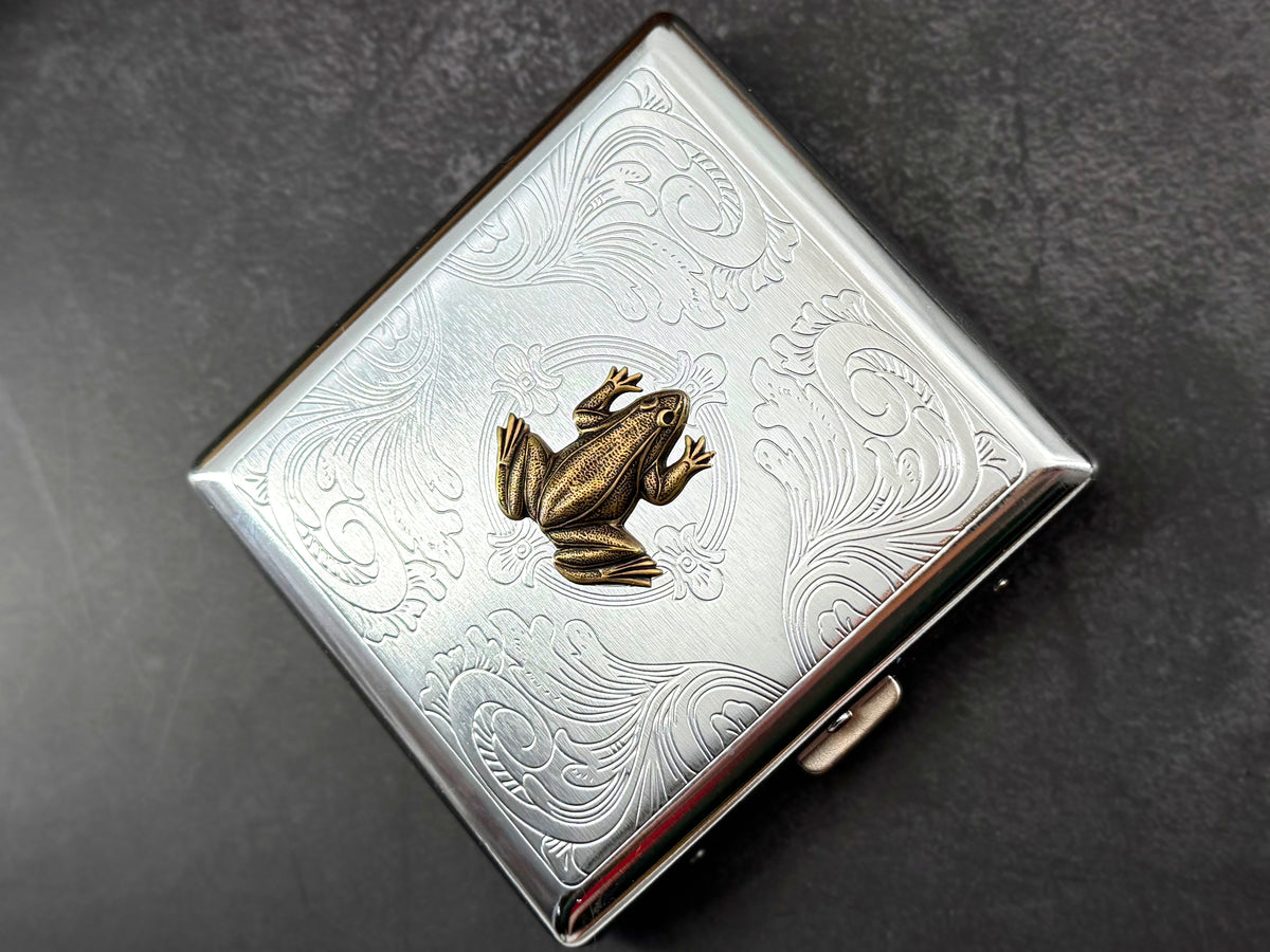 Bronze frog card holder featuring decorative floral scrollwork on a silver case.