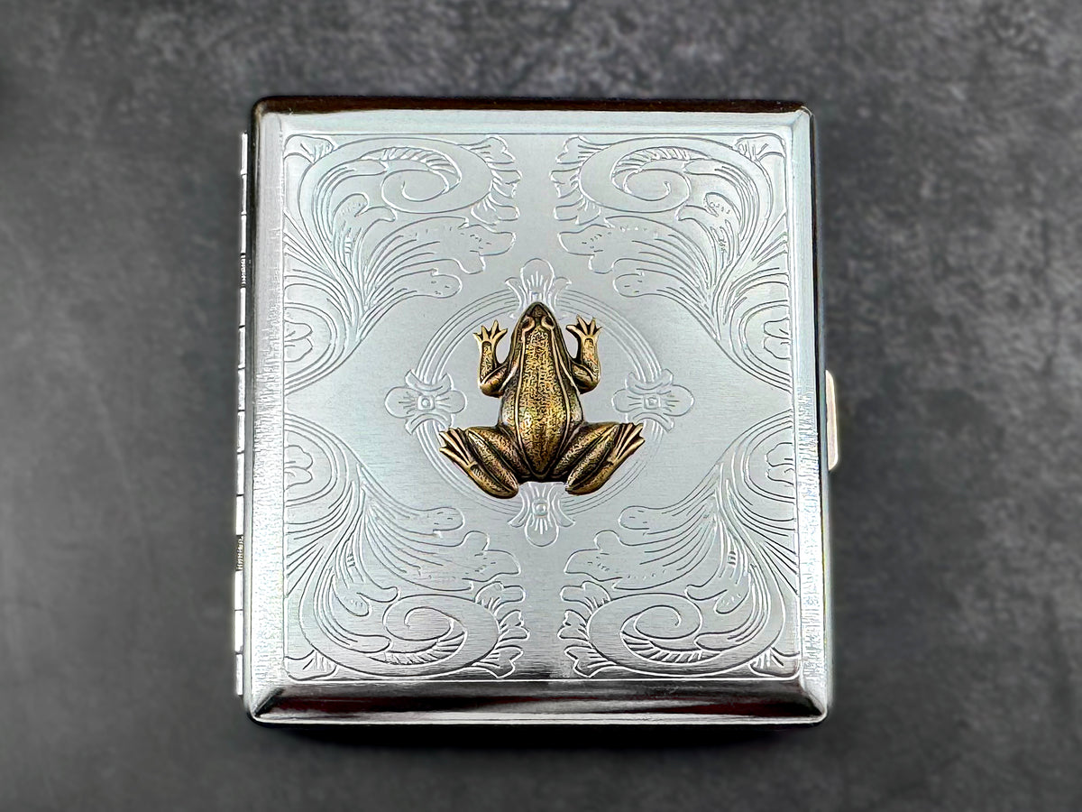 Handmade frog cigarette case photographed against a dark textured background.