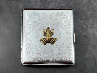 Handmade frog cigarette case photographed against a dark textured background.