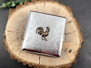 Angled view of handmade metal cigarette case with raised rooster design.