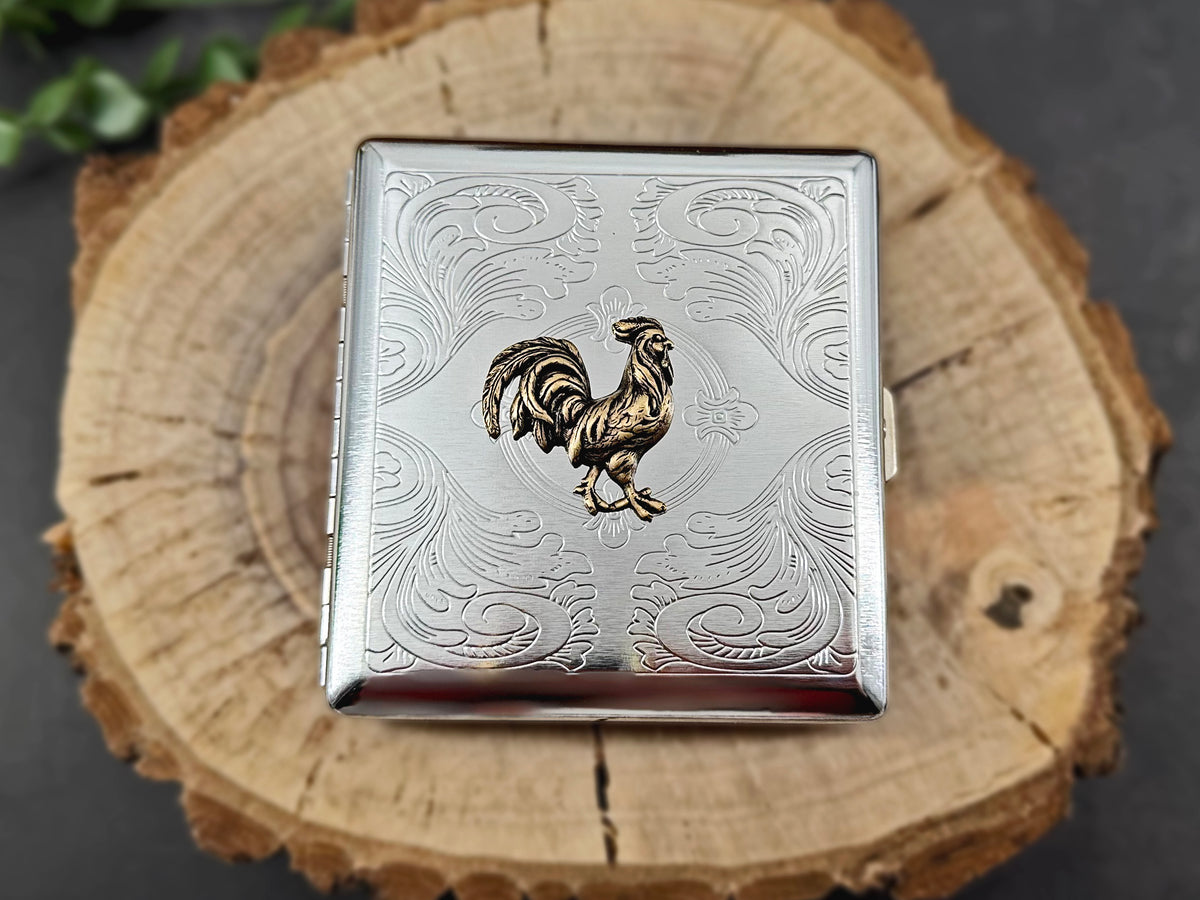 Bronze rooster card holder with intricate floral scrollwork on a silver metal case.