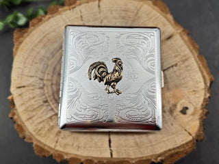 Bronze rooster card holder with intricate floral scrollwork on a silver metal case.