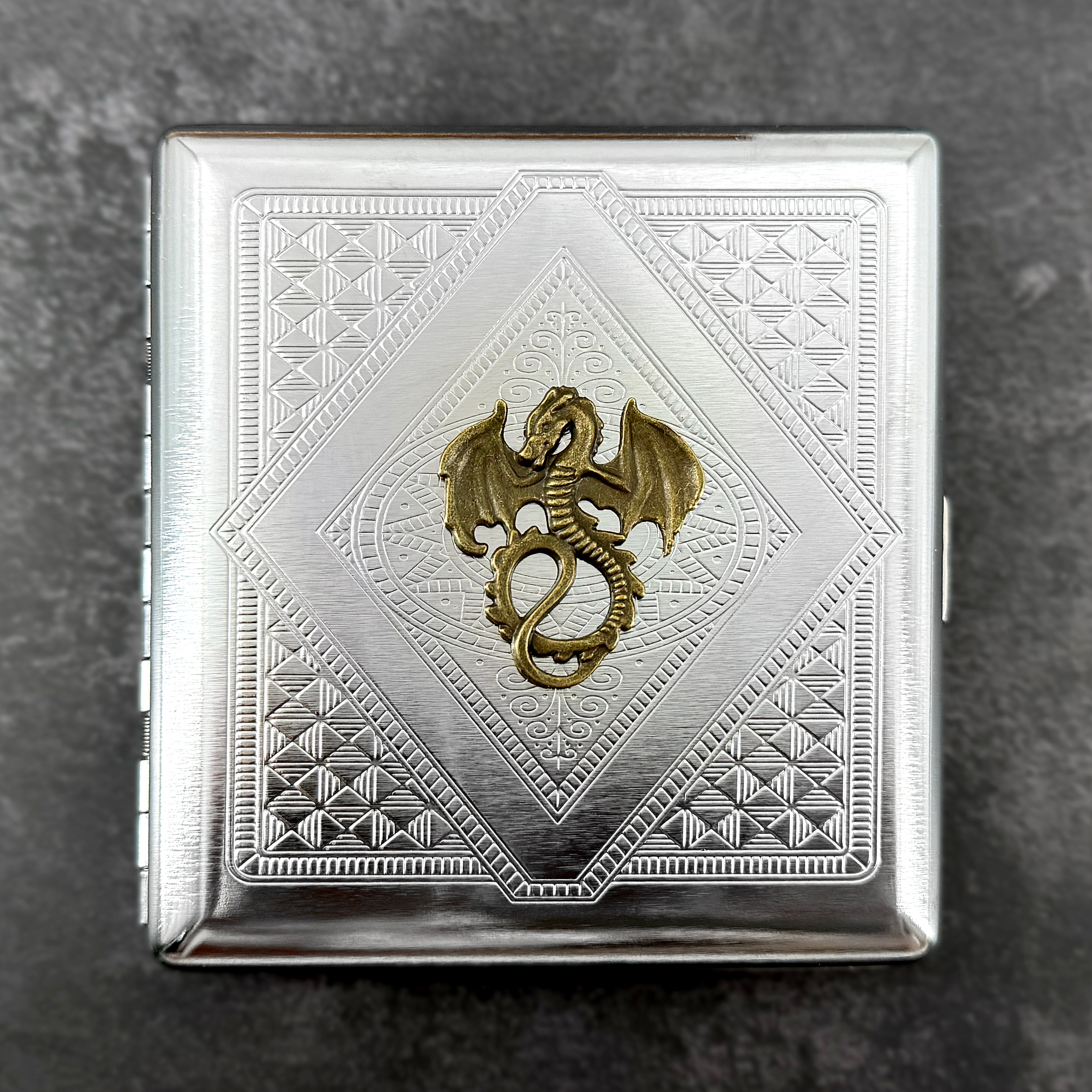 Close-up of antique bronze winged dragon on stamped metal cigarette case