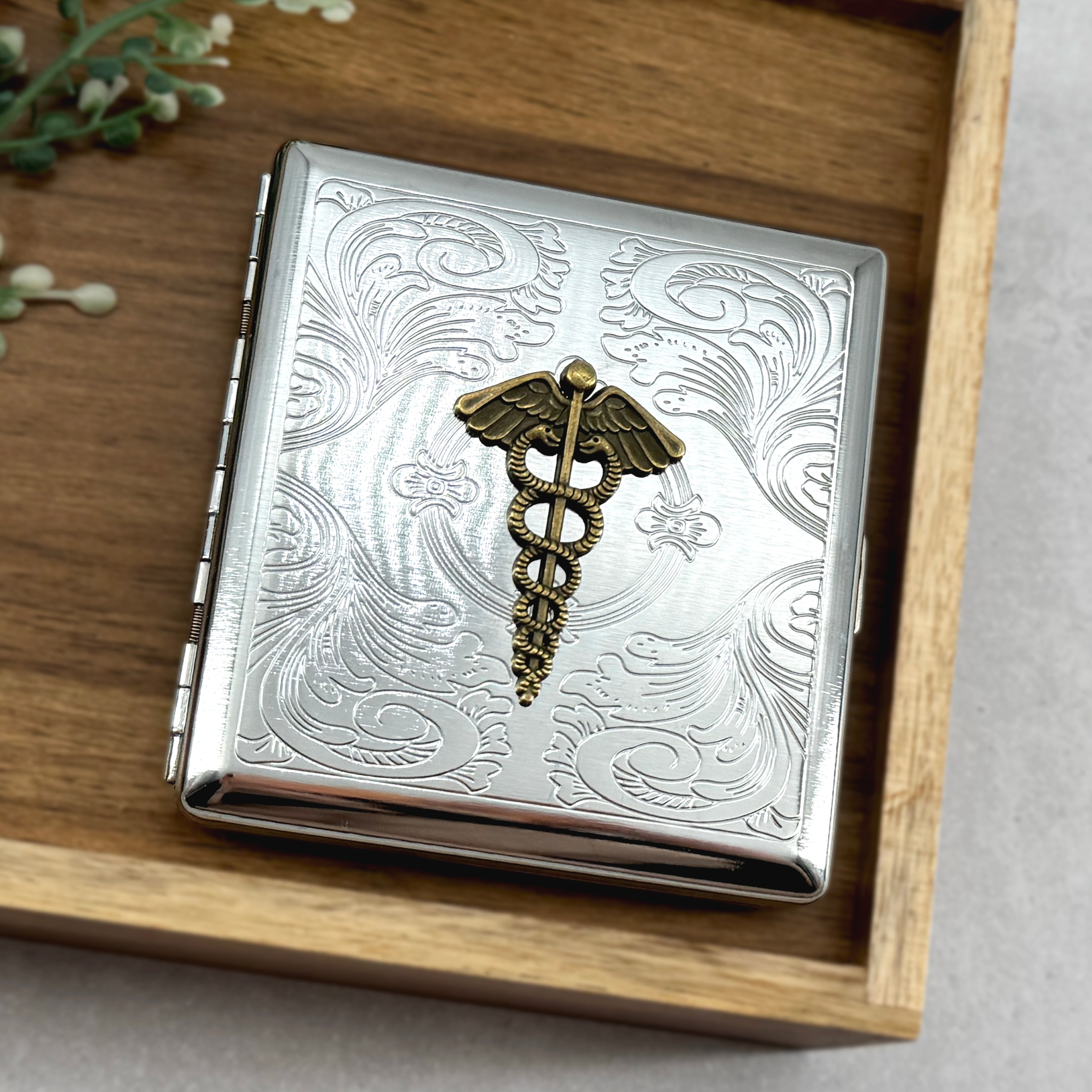 Metal cigarette and card holder featuring bronze caduceus emblem on silver finish