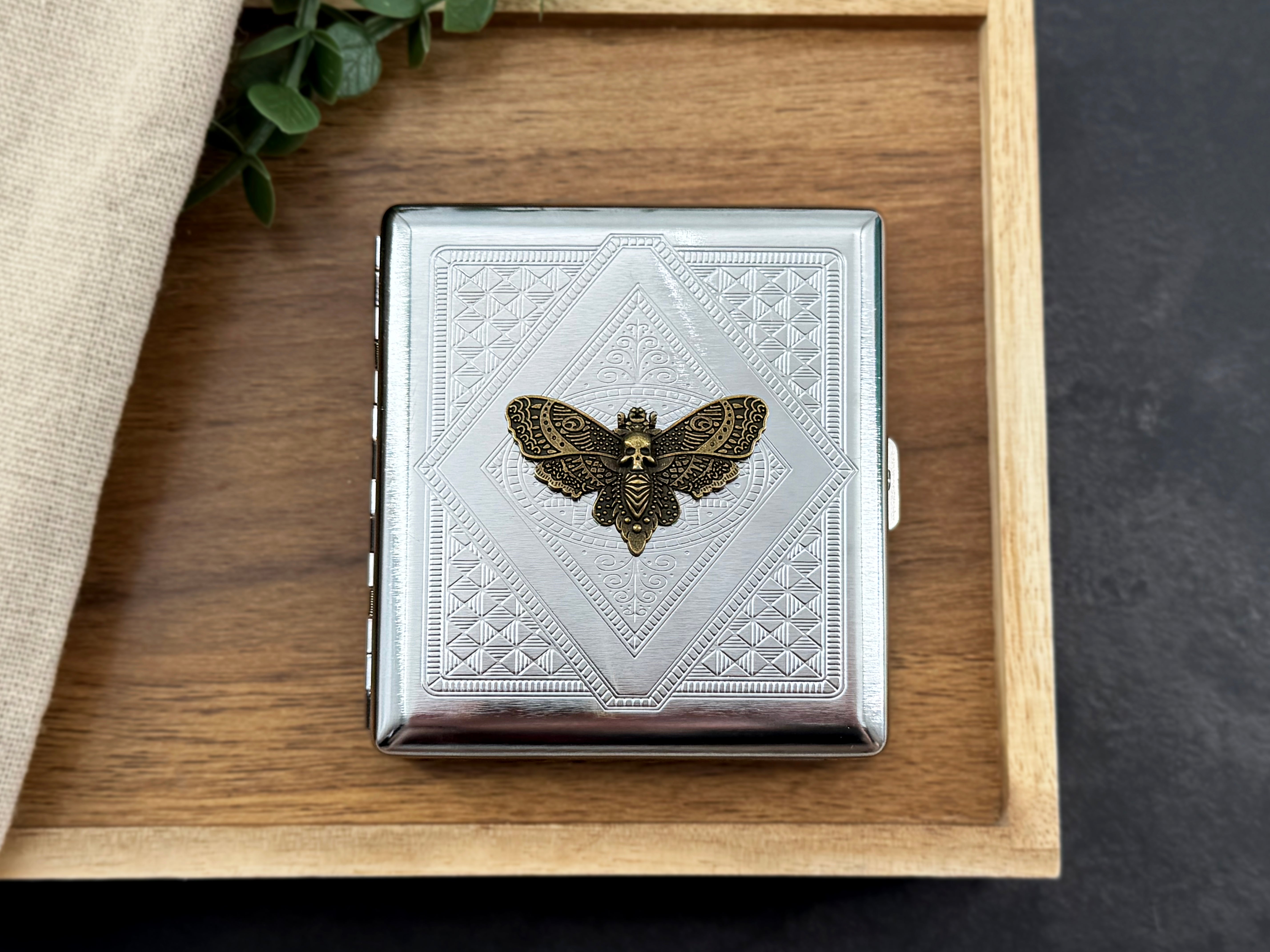 Close-up of antique-bronze-toned Death’s-head hawkmoth detail on a stamped metal case