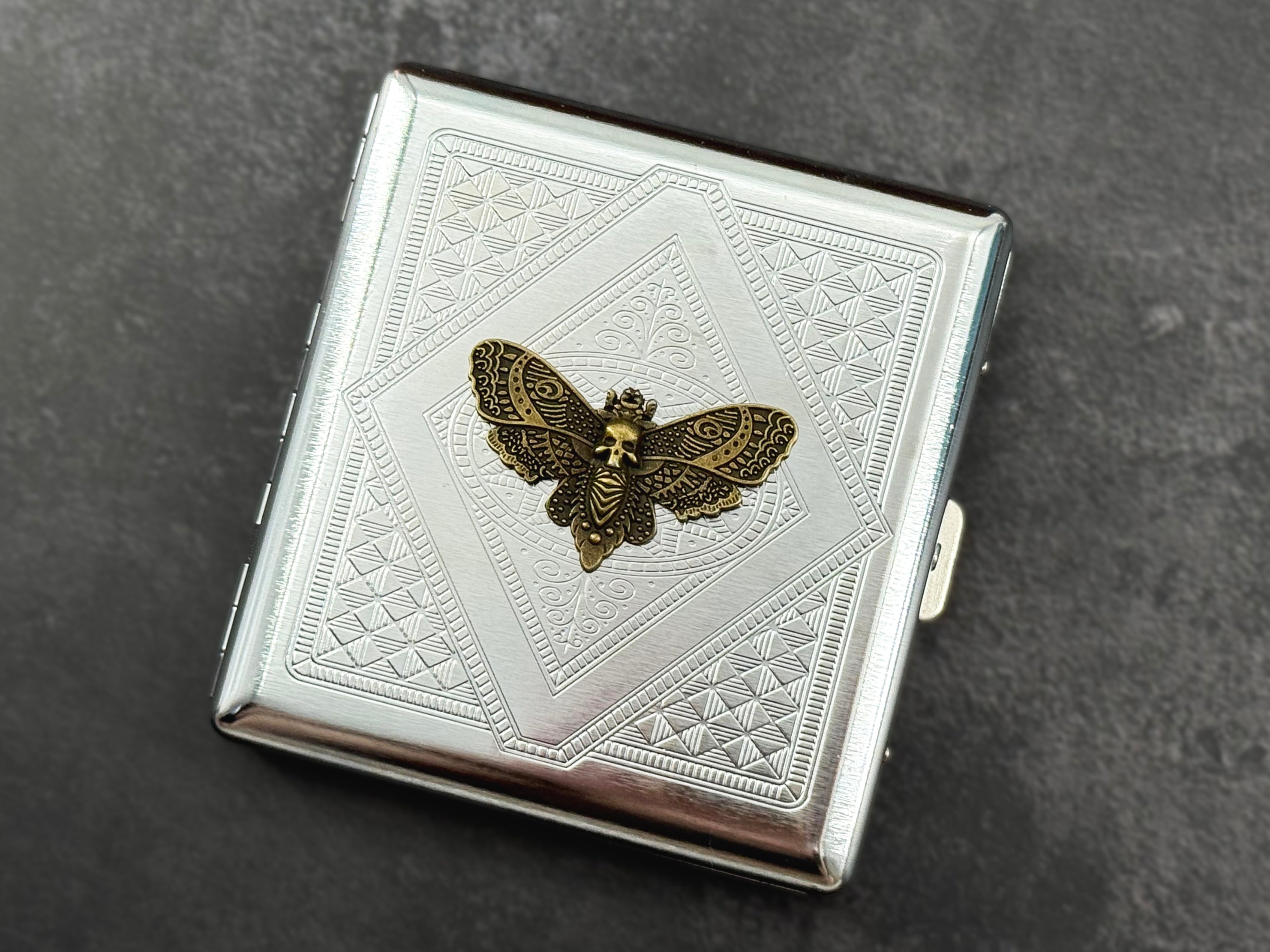 Geometric Death’s-head moth cigarette case photographed at an angle on a dark background