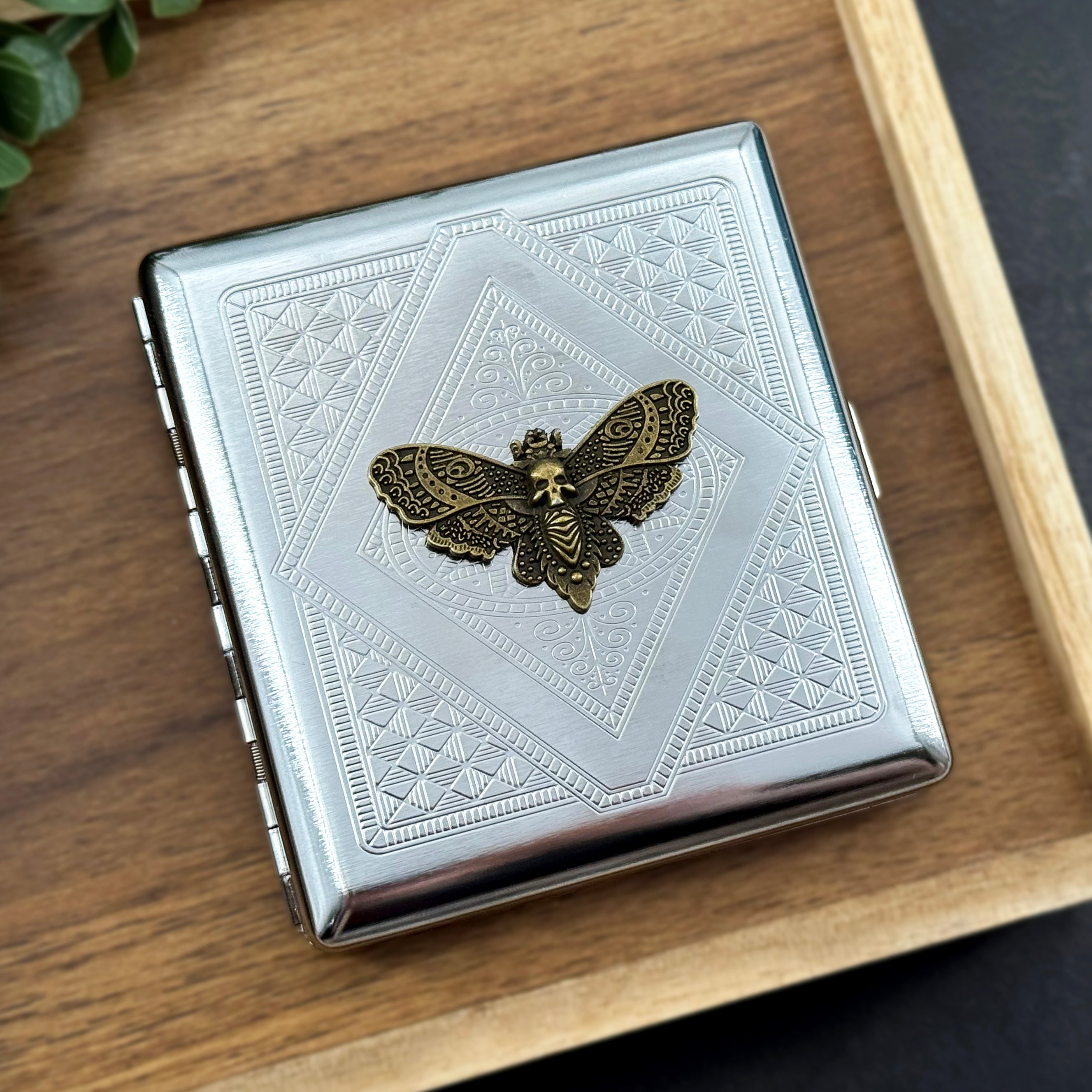 Front view of silver metal card holder with raised hawkmoth and detailed geometric stamping