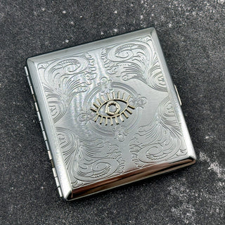 Evil eye cigarette case with engraved scrollwork pattern on dark stone background