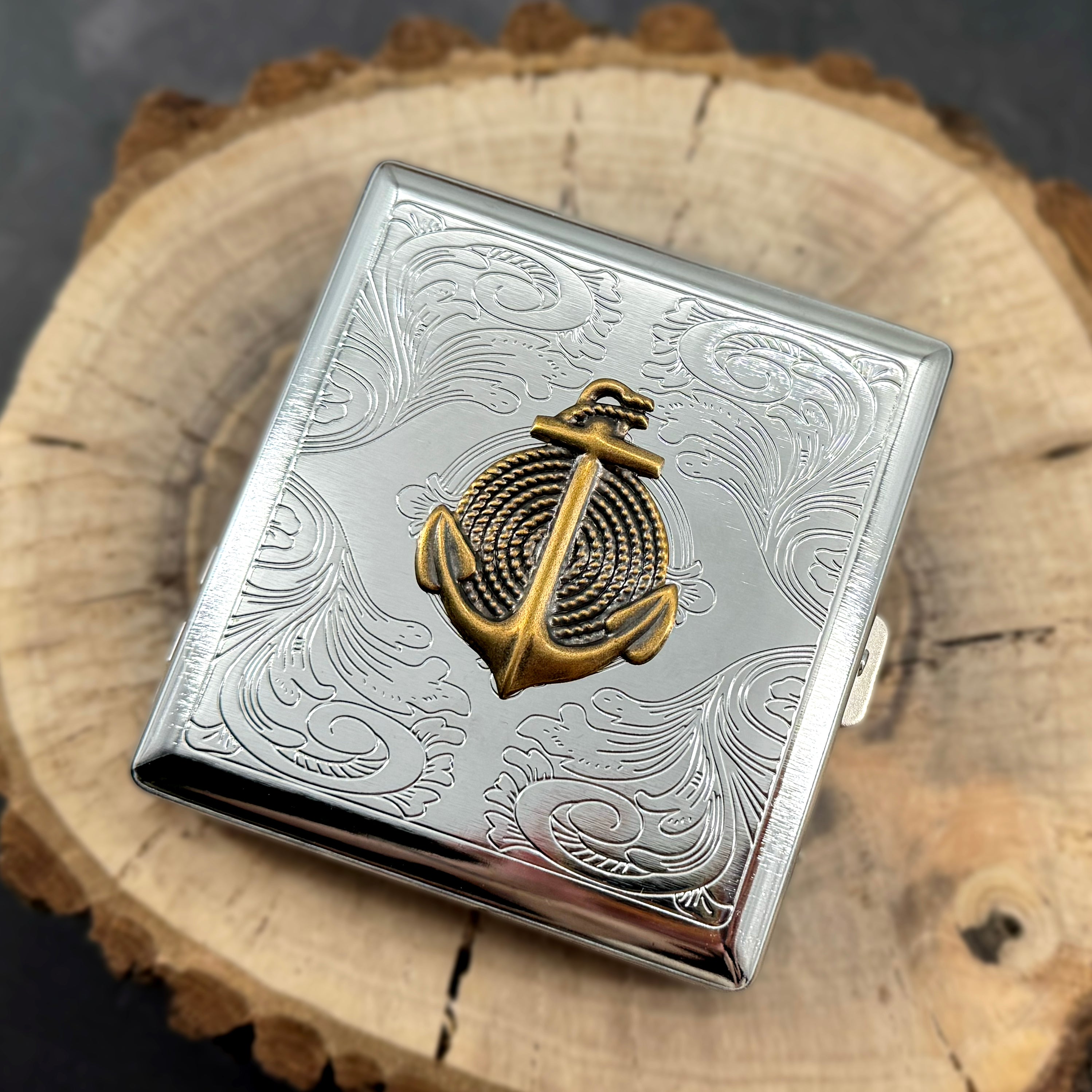 Silver cigarette case featuring gold nautical anchor and ornate scrollwork