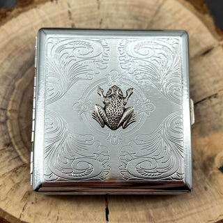 Silver cigarette case featuring a raised frog on a stamped metal scrollwork background.