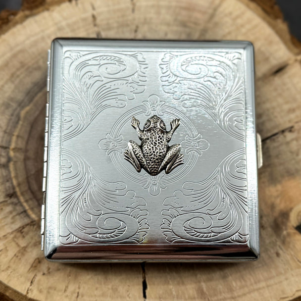 Silver cigarette case featuring a raised frog on a stamped metal scrollwork background.