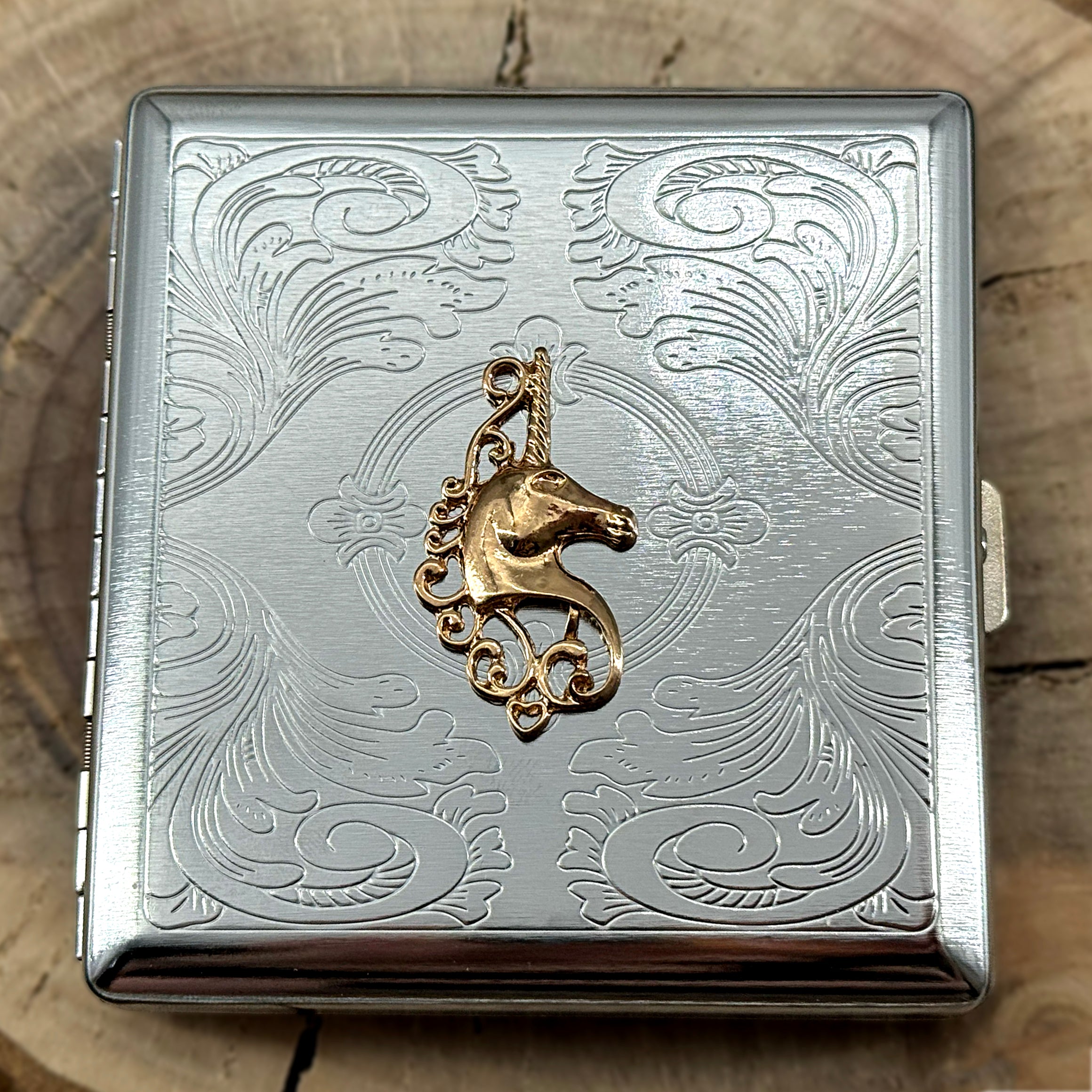Fantasy-themed metal cigarette case with an ornate stamped metal scrollwork background.
