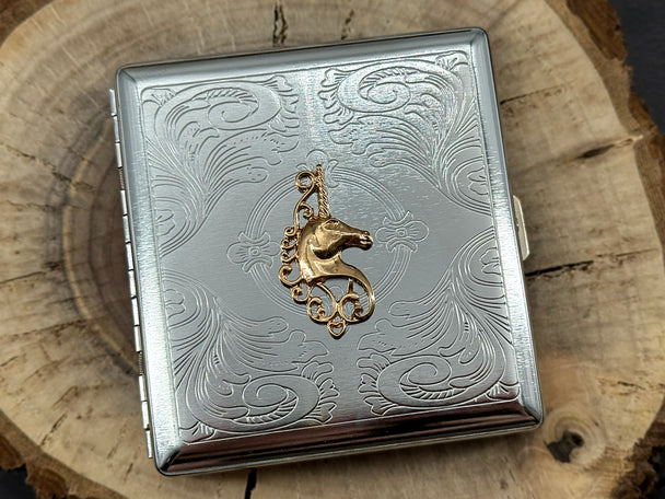 Silver cigarette case with a raised gold unicorn on a stamped metal scrollwork background.