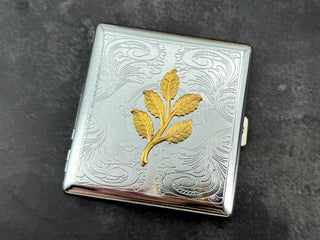 Metal business card holder with raised gold leaves and ornate stamped background.