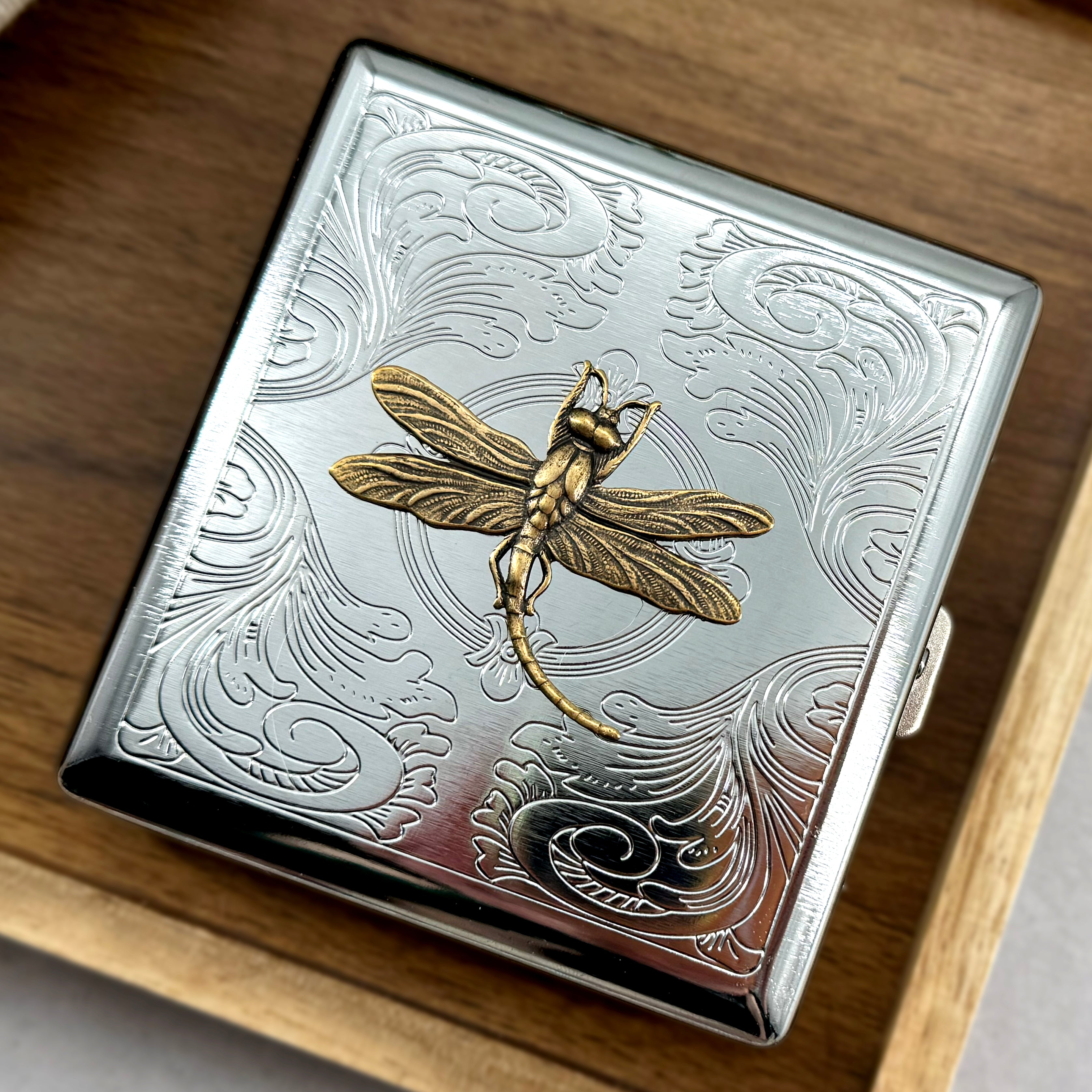 Stamped metal cigarette case with raised golden dragonfly design and ornate scrollwork