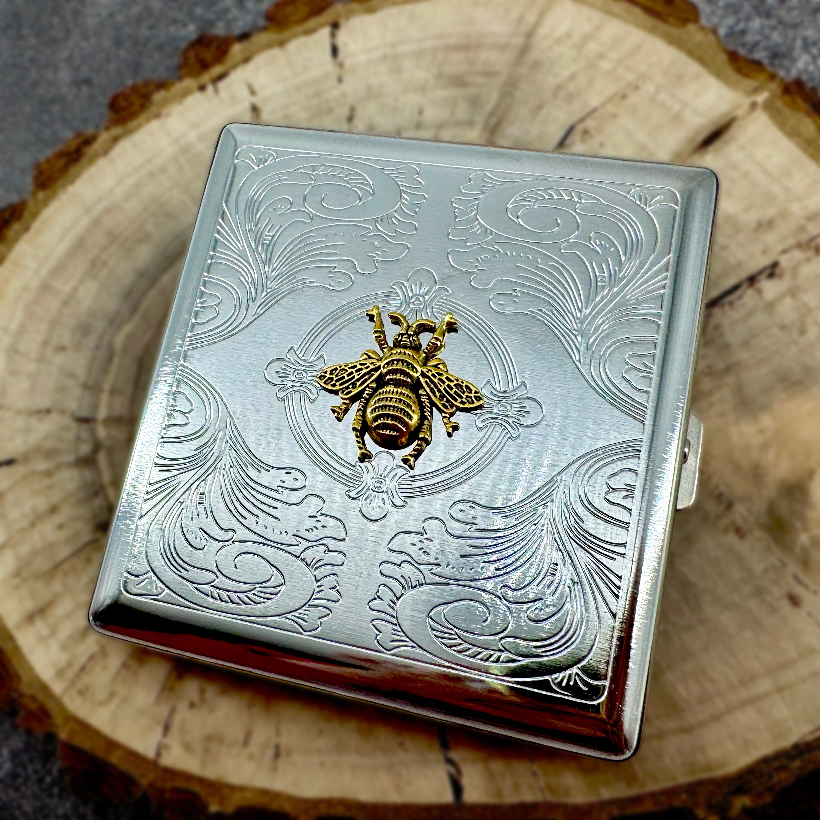 Silver pocket case featuring ornate stamped background and gold bee detail