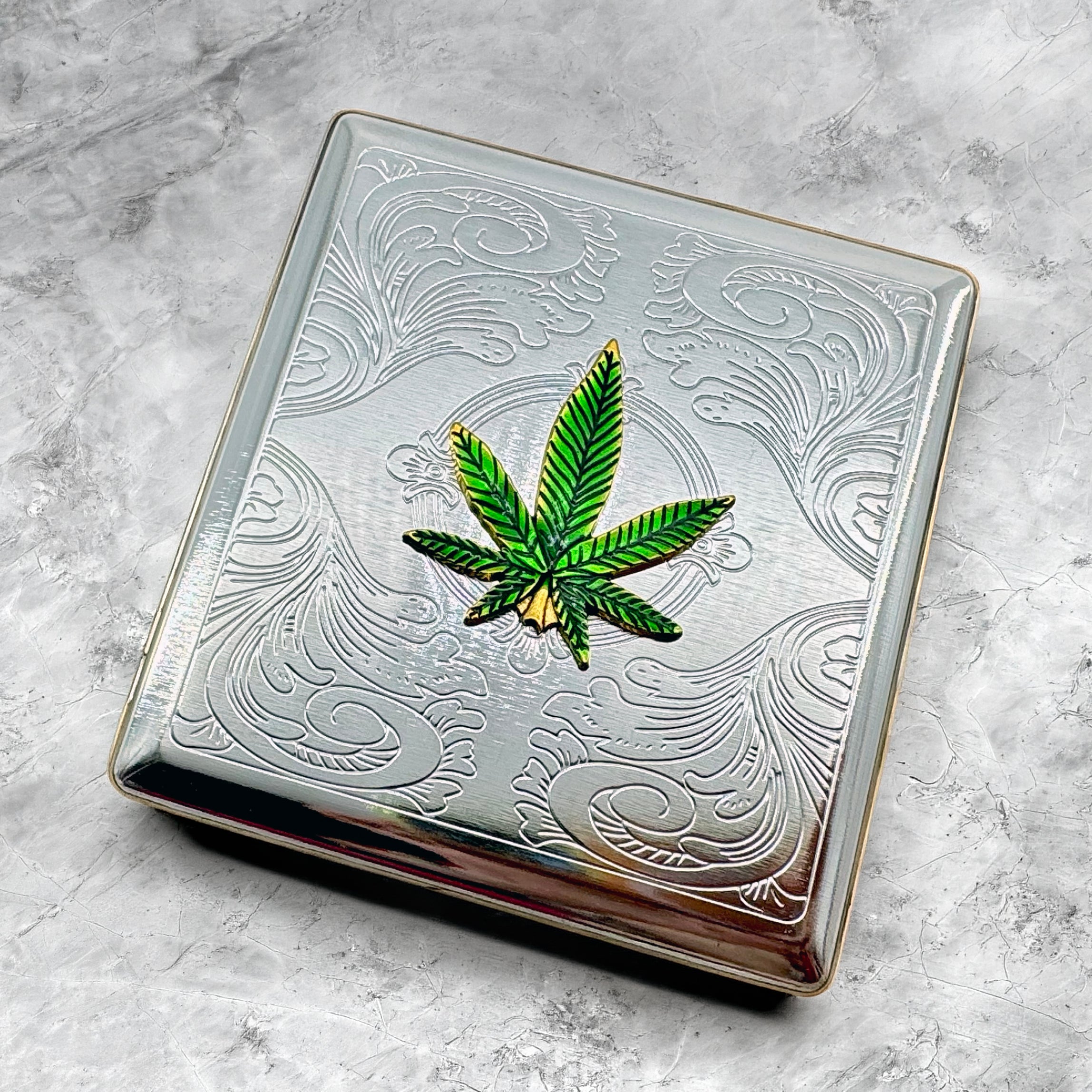 Green cannabis leaf cigarette case displayed on stone background