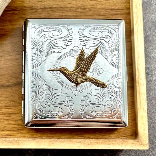 Golden hummingbird pocket case displayed on a wooden tray