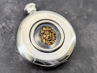 Angled view of lion hip flask showing raised metallic lion head and transparent center window