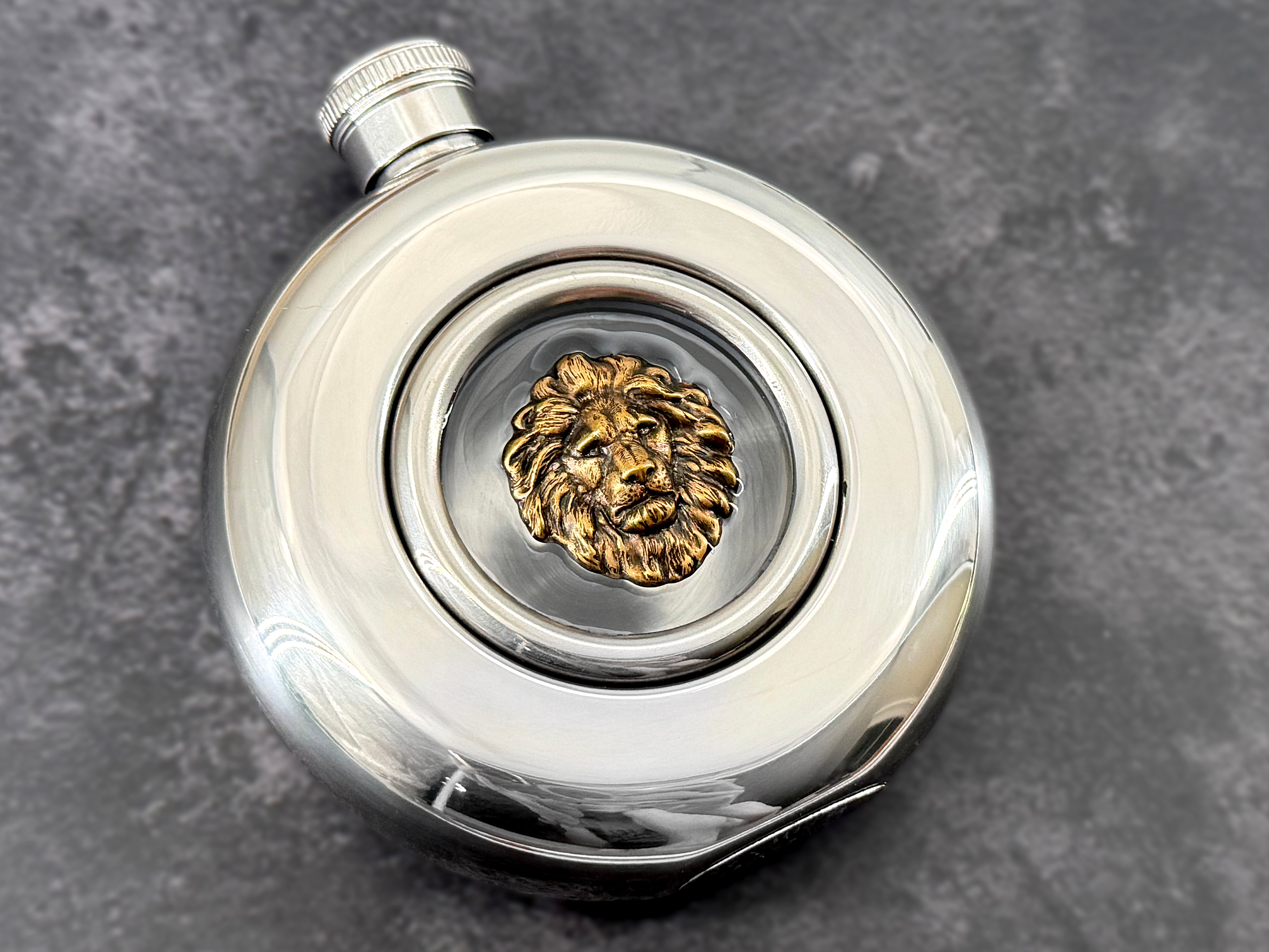 Angled view of lion hip flask showing raised metallic lion head and transparent center window