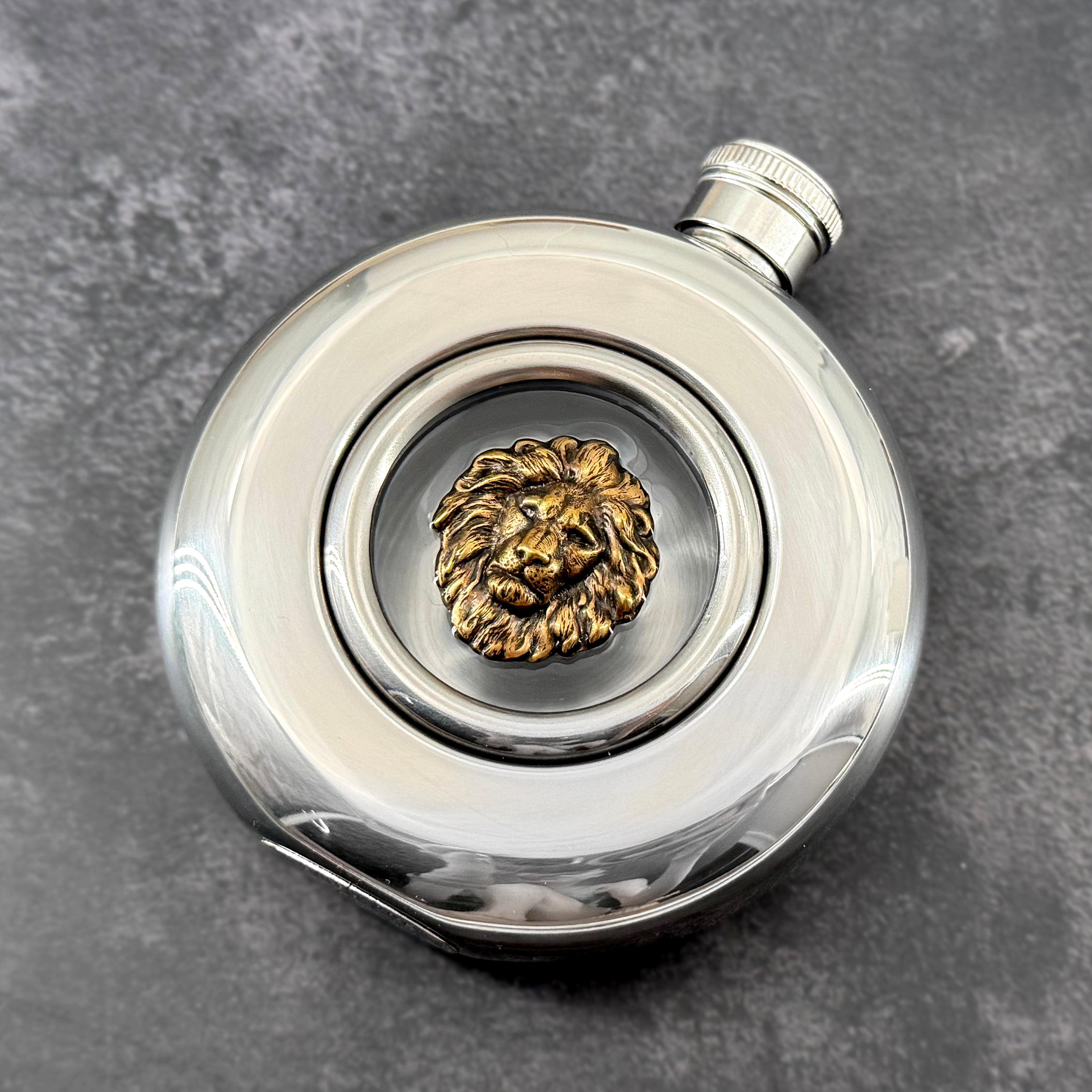 Regal round window flask featuring an antique bronze-toned lion motif and polished stainless steel body
