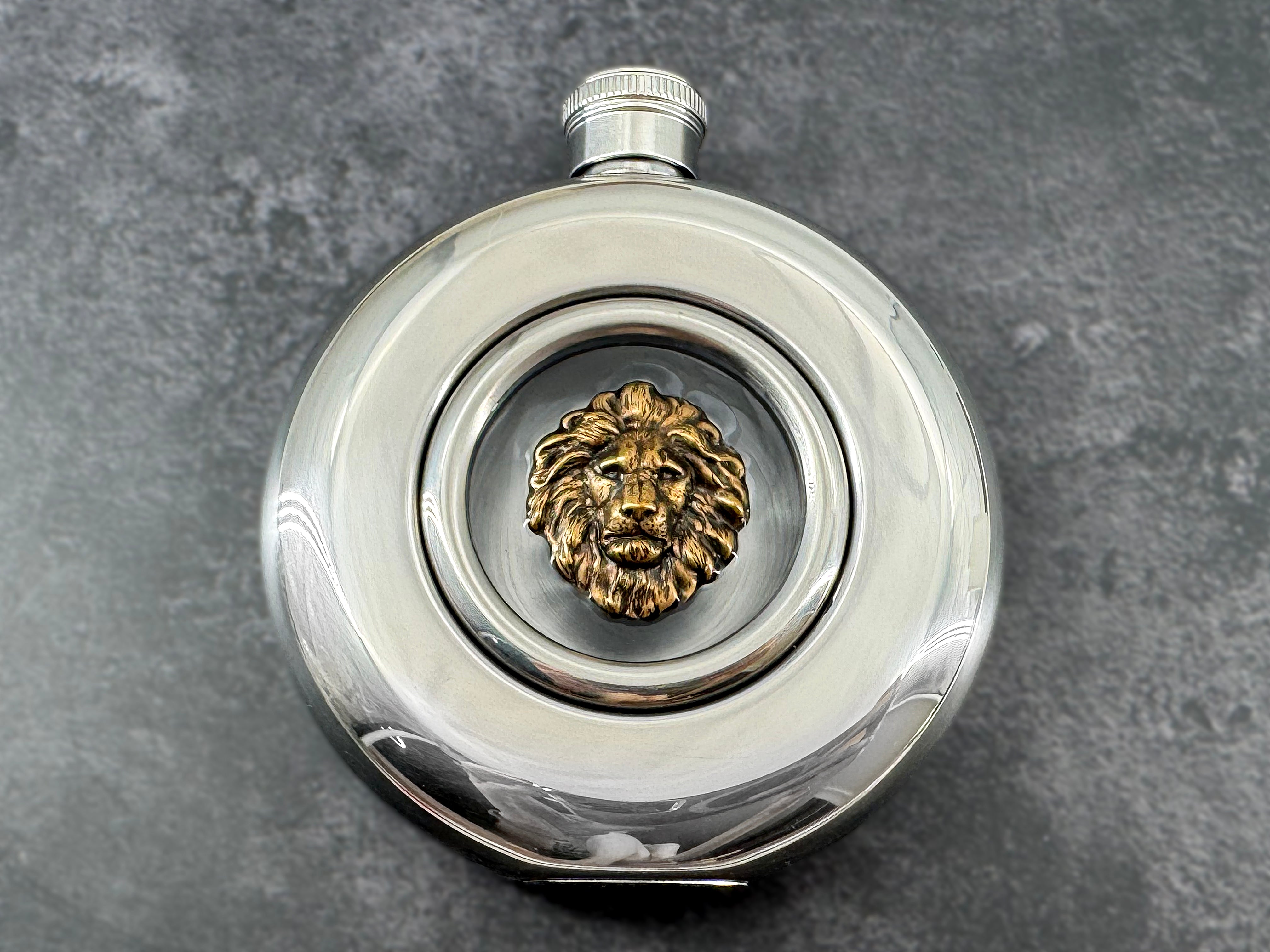 Lion flask with antique bronze-toned lion head centered in a clear circular viewing window