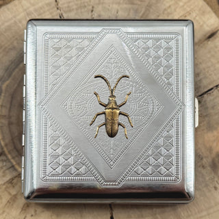 Longhorn beetle metal cigarette case featuring a raised beetle on an intricate geometric stamped background