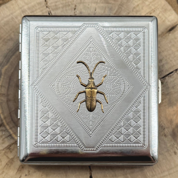 Longhorn beetle metal cigarette case featuring a raised beetle on an intricate geometric stamped background