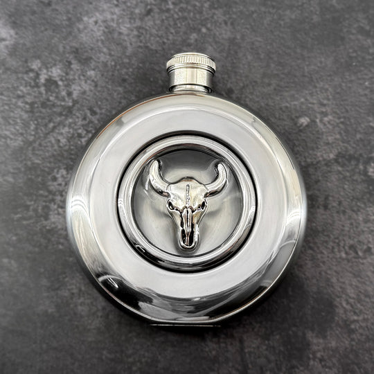 Round stainless steel flask with raised silver longhorn skull and clear circular viewing window