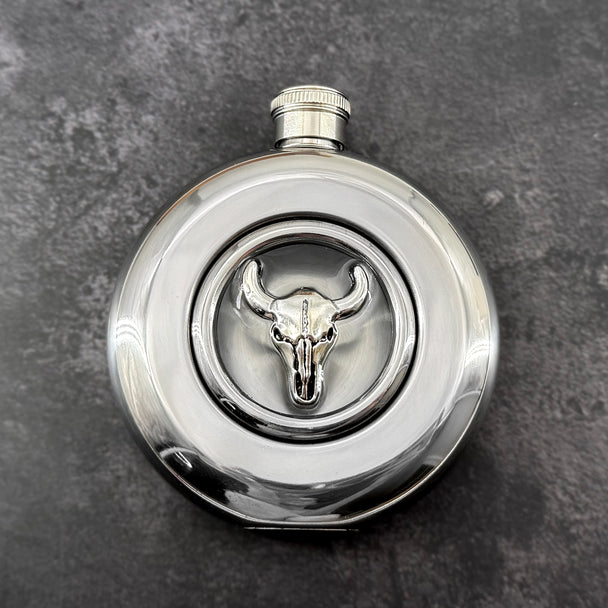 Round stainless steel flask with raised silver longhorn skull and clear circular viewing window