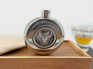 Longhorn skull flask photographed on a wooden tray with whiskey glass in the background