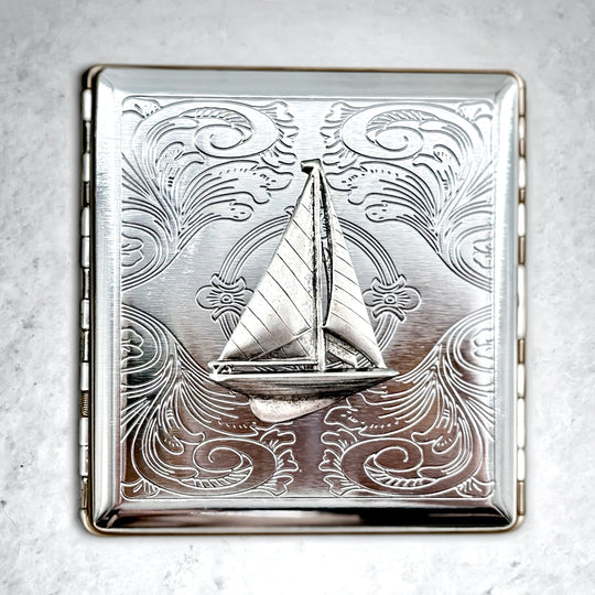 Sailboat cigarette case with raised nautical design and engraved scrollwork