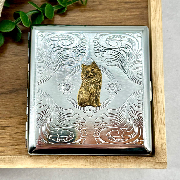 Silver stamped metal cigarette case with raised Persian cat charm on ornate background