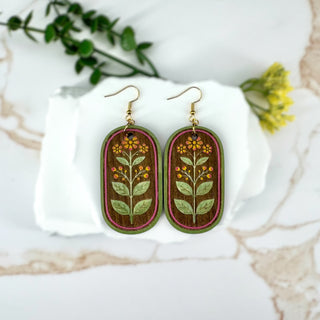 Pair of earrings with floral design on a white surface with greenery in the background