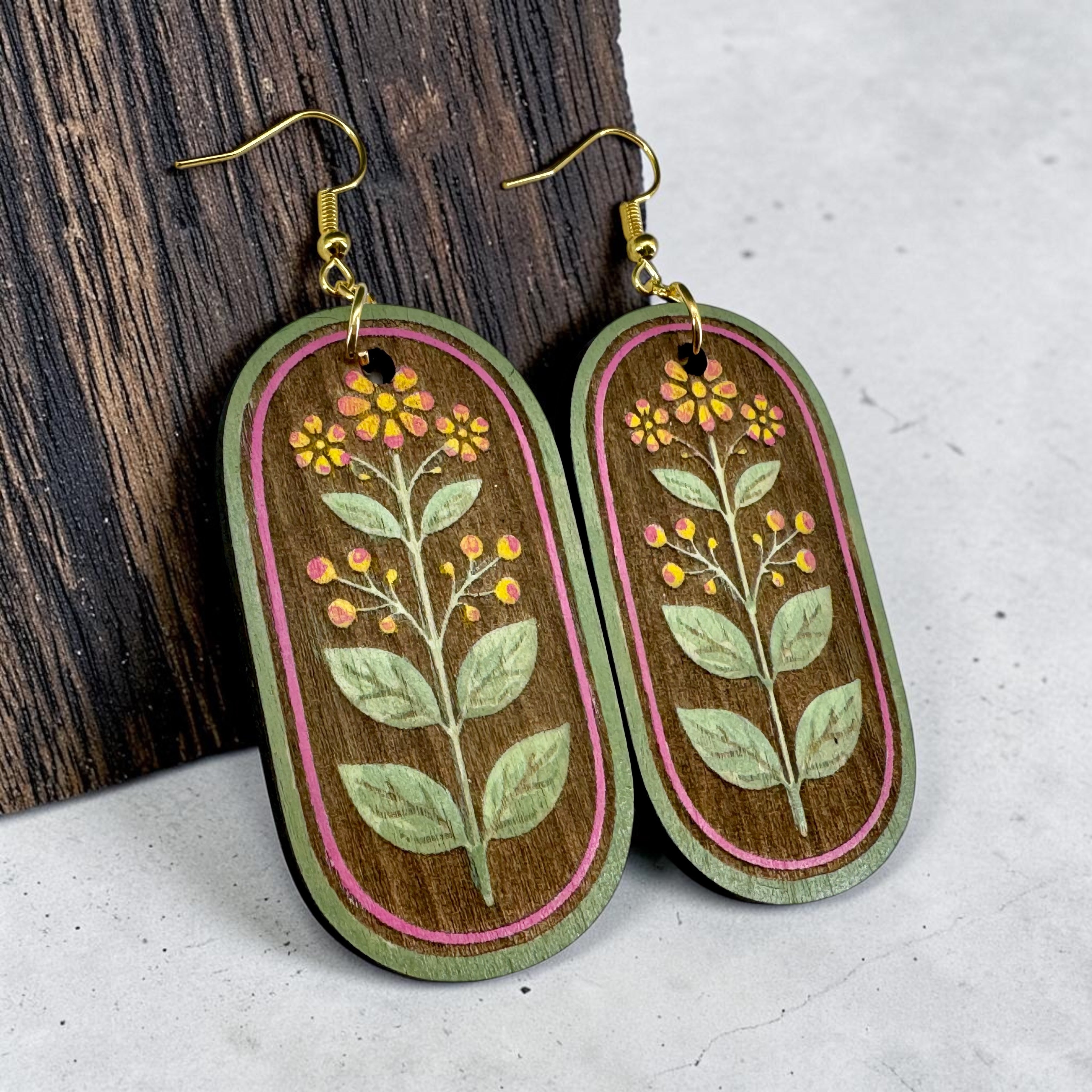 Oval-shaped wooden earrings with floral designs on a wooden and gray surface.