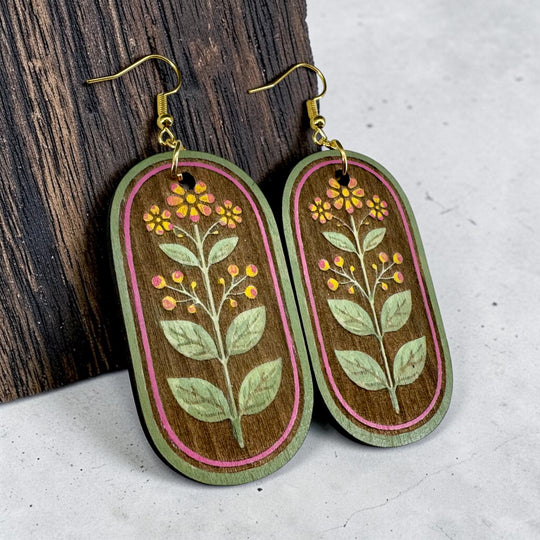 Oval-shaped wooden earrings with floral designs on a wooden and gray surface.