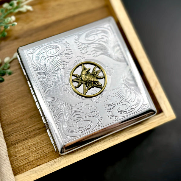 Raven pocket case featuring a raised raven and pentacle design on engraved silver metal