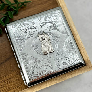 Front view of metal cat cigarette case with ornate scrollwork background
