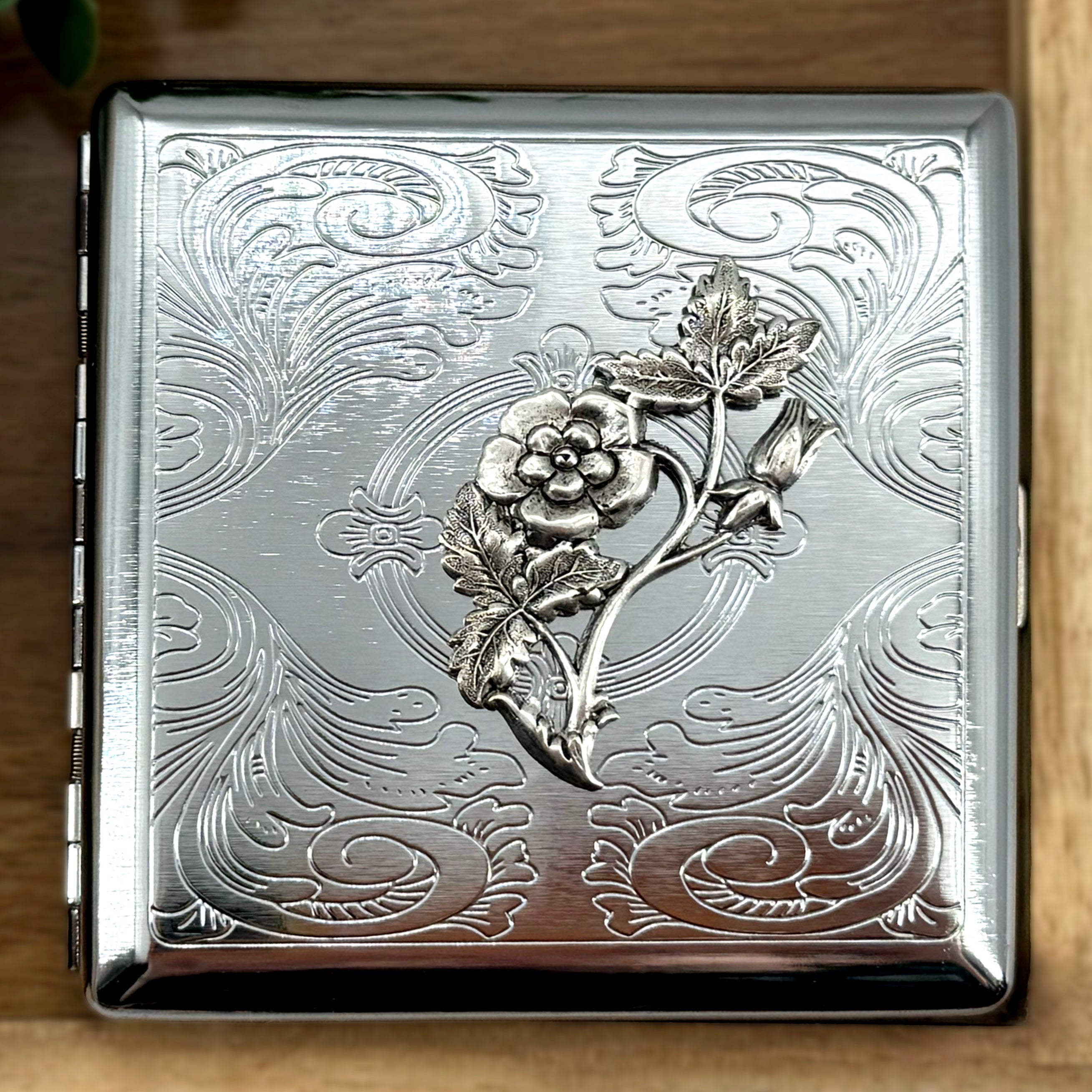 Silver metal cigarette case with raised floral vine design and ornate scrollwork