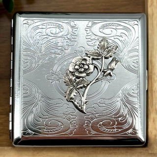 Silver metal cigarette case with raised floral vine design and ornate scrollwork