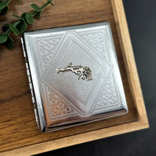 Wild Rose cigarette case with raised revolver and rose on silver stamped metal background