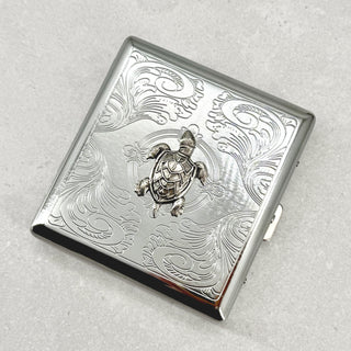 Angled view of sea turtle metal cigarette case with ornate stamped scrollwork design