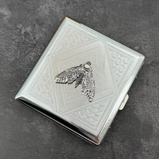 Silver moth cigarette case with dark recessed details and geometric metal background